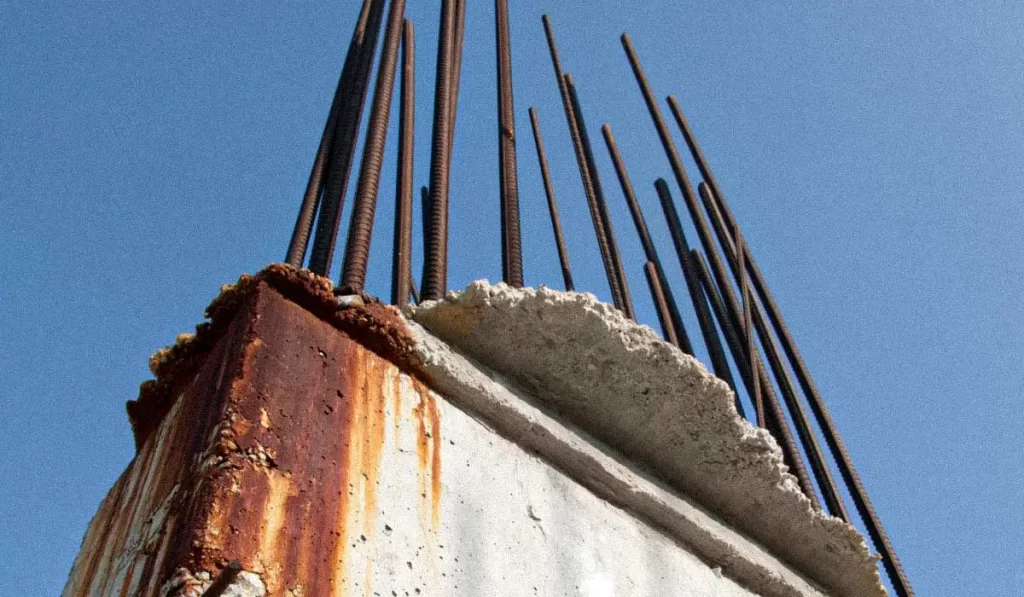 a imagem tem um pilar com barras de espera (armadura de arranque) com sinais de corrosão.