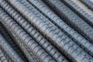 A imagem possui várias barras de aço bem próximas, onde é possível verificar suas ranhuras. A imagem é a capa de um artigo que ensina como calcular o peso das barras de aço