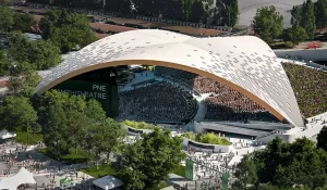 Render: Vista aérea do Freedom Mobile Arch (Maior telhado de madeira autoportante do mundo) concluído, com cobertura curva em madeira engenheirada de 105 metros de vão livre, público reunido no anfiteatro e parque ao redor.